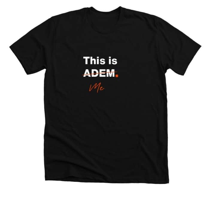 Black t-shirt with This is ADEM in white text. ADEM is crossed out with orange ink and beneath is the word Me in orange text.