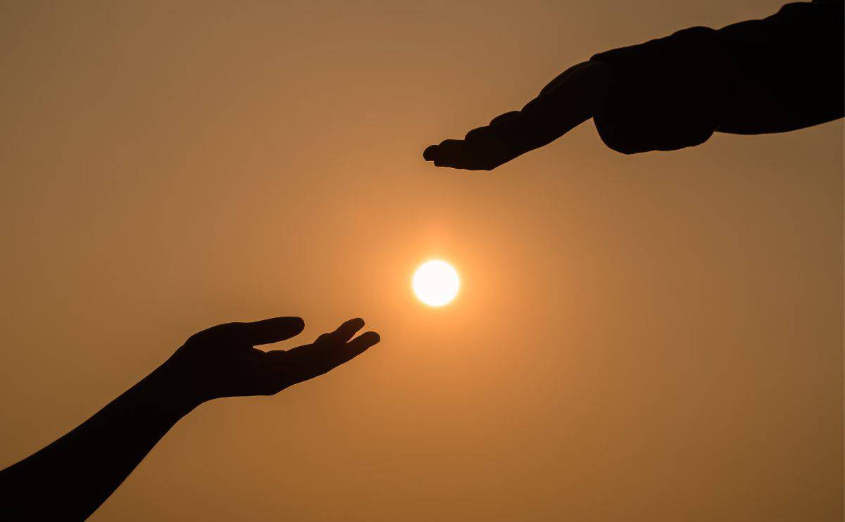 Silhouette of two hands about to touch with the sun in the background