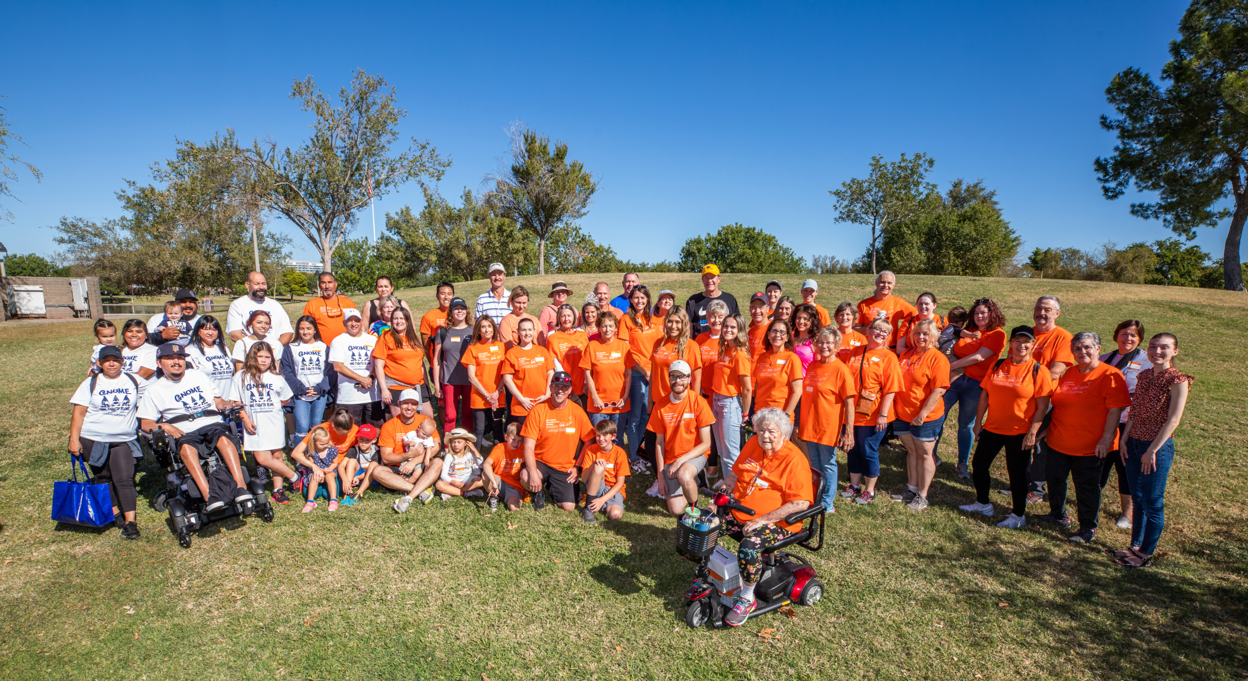 Group photo from Arizona Walk-Run-N-Roll. Group of people in bright orange shirts on grass with a clear blue sky above.