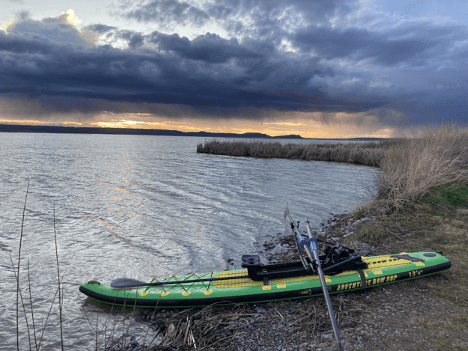 Photo of a green and yellow paddle board on the bank of a reservoir at sunset.