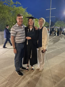 Picture of Tara standing between her parents, wearing a cap and gown.